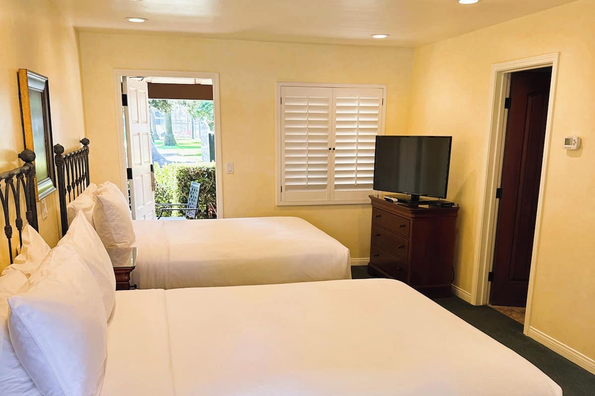 A hotel room with two beds, a television, a dresser, and a window with blinds.