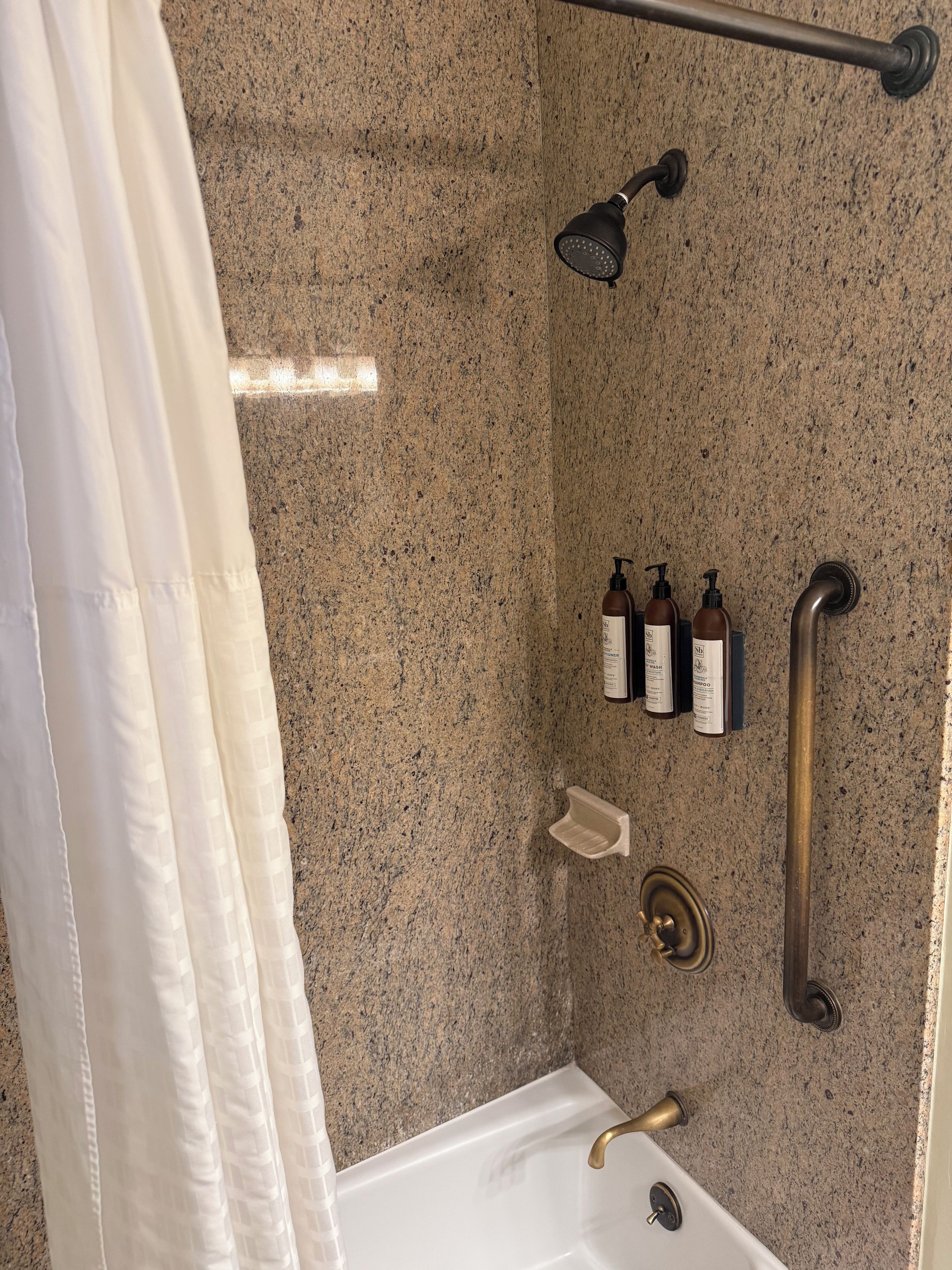 Une salle de bain équipée d’une douche, d’une baignoire, d’une barre d’appui et d’articles de toilette.