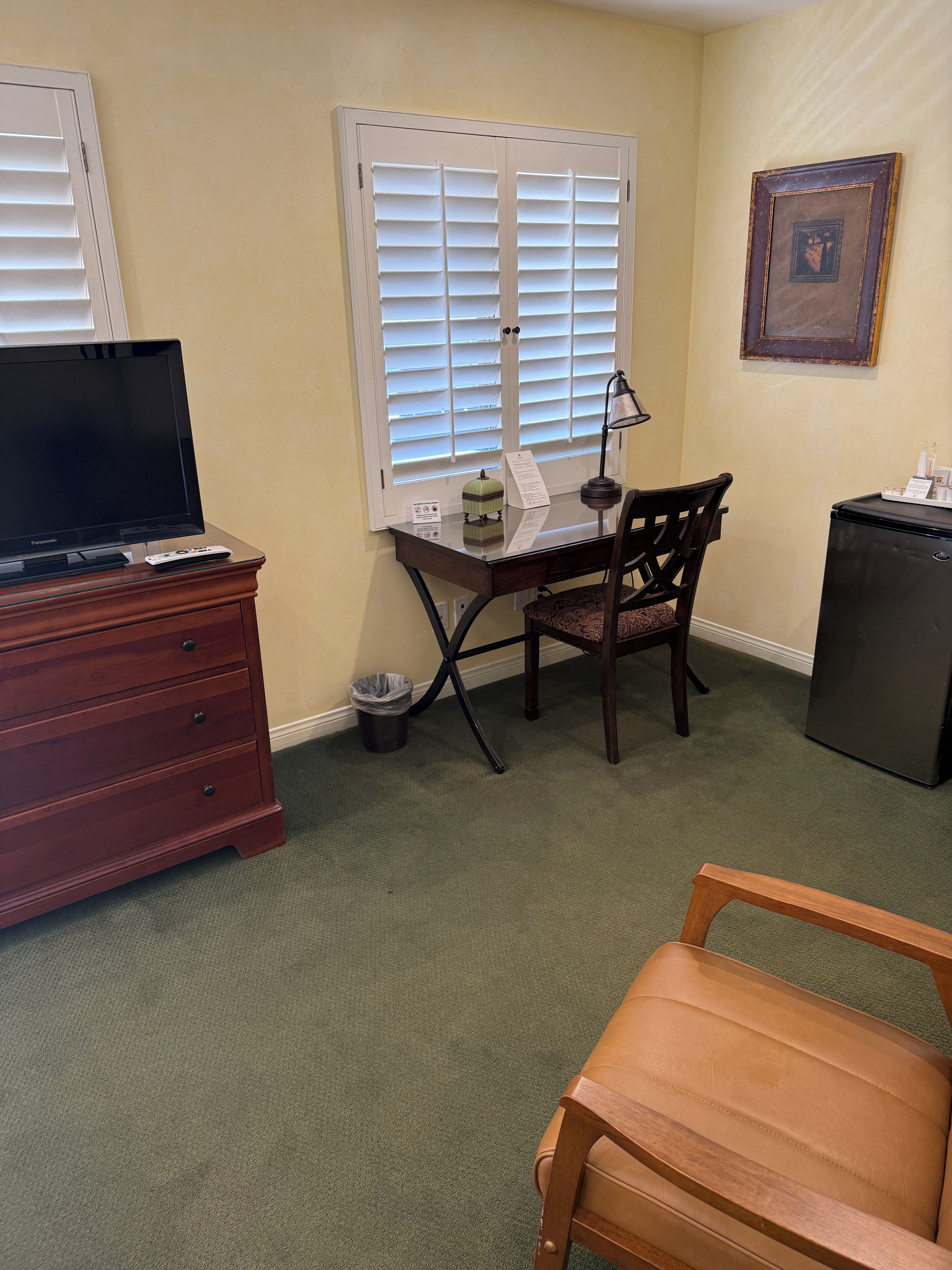 Una habitación con televisión, escritorio, silla y un basurero.