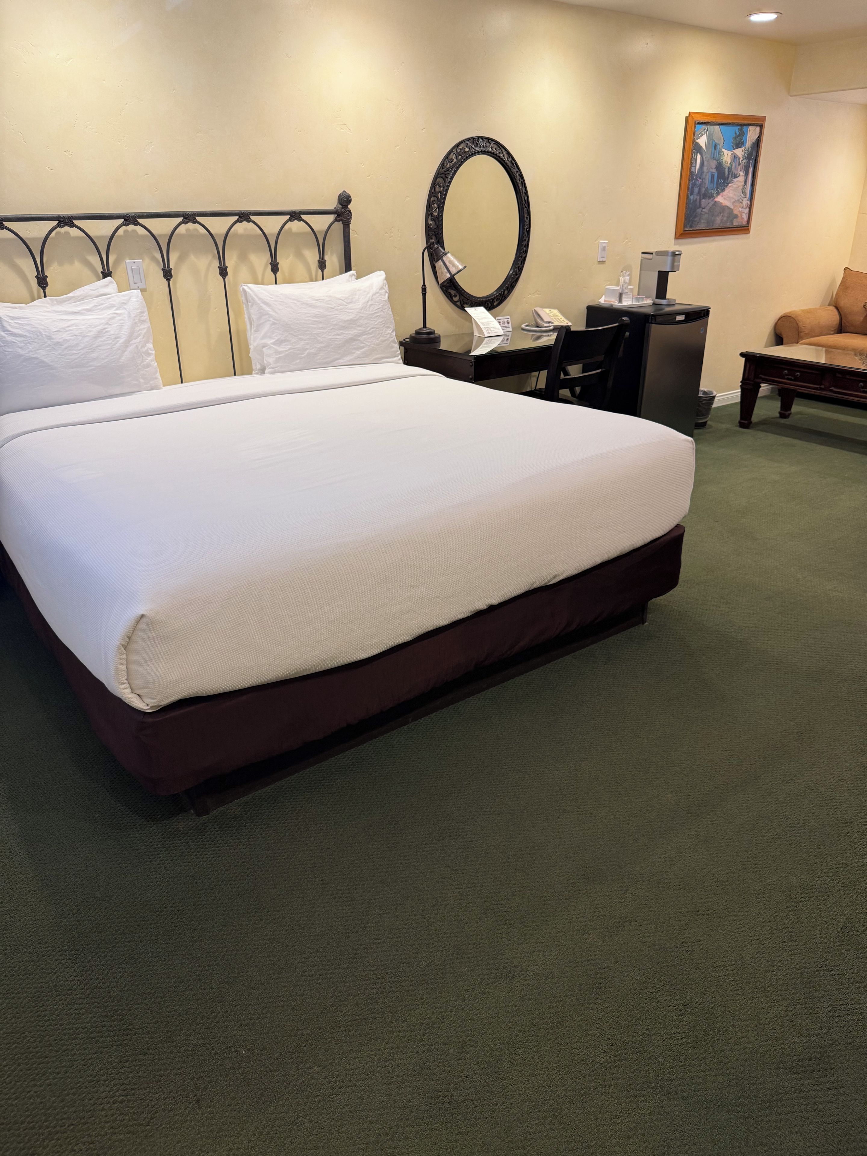 A hotel room with a large bed, a desk with a telephone, a mirror, and a painting on the wall.