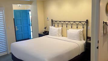 Una habitación de hotel con una cama grande, una mesita de noche, una lámpara y una puerta.