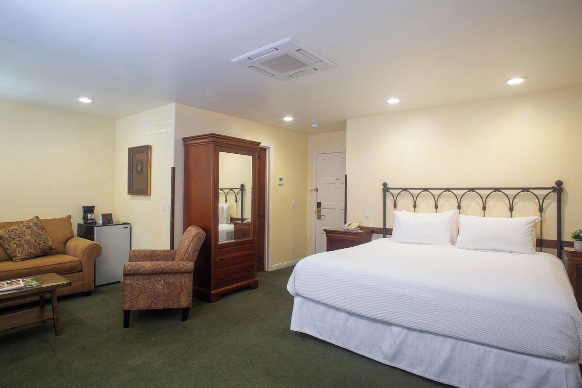A hotel room with a bed, a sofa, a chair, a dresser, and a small desk.