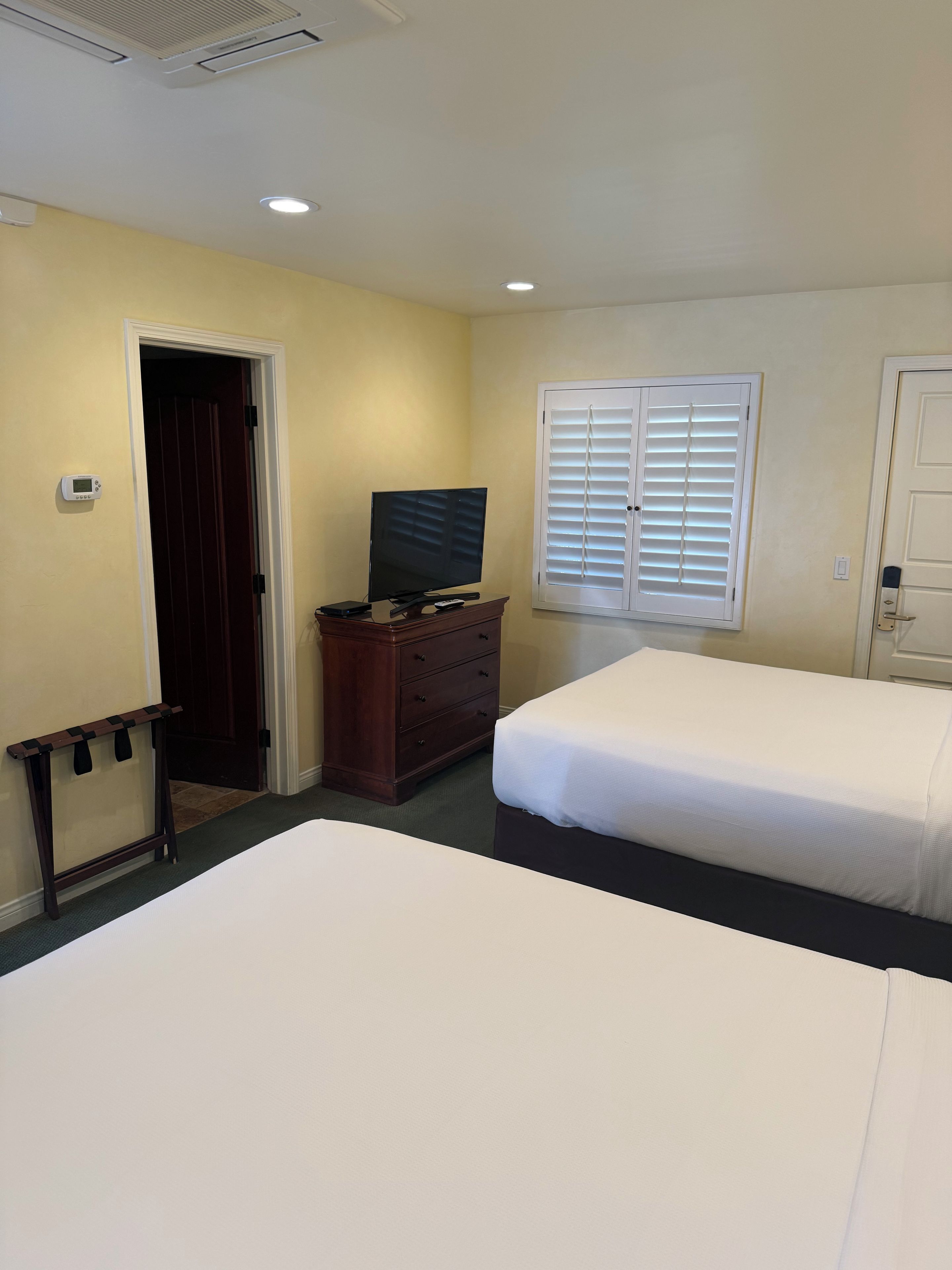 A hotel room with two beds, a dresser, a television, and a window with blinds.