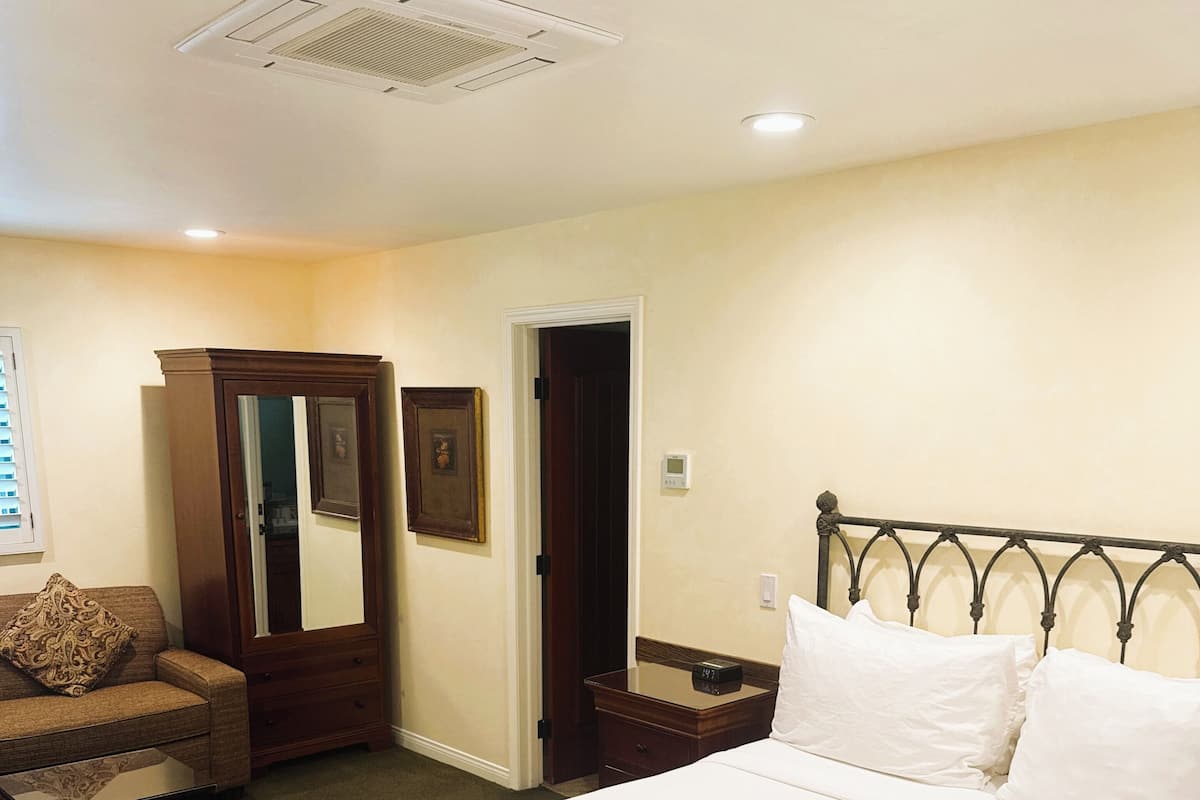 A hotel room with a large bed, a wooden wardrobe, a small table, a chair, and a mirror.