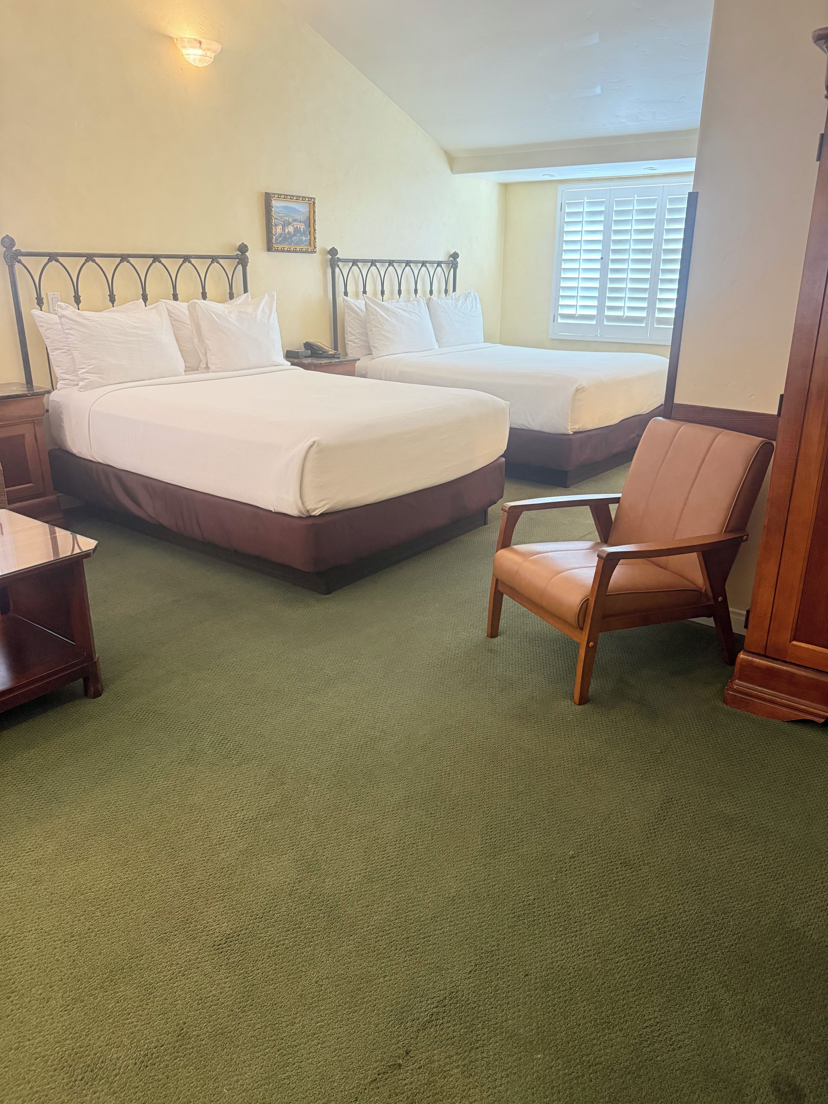 Ein Hotelzimmer mit zwei Betten, einem Holzbettchen, einem Nachttisch und einem grünen Teppich.