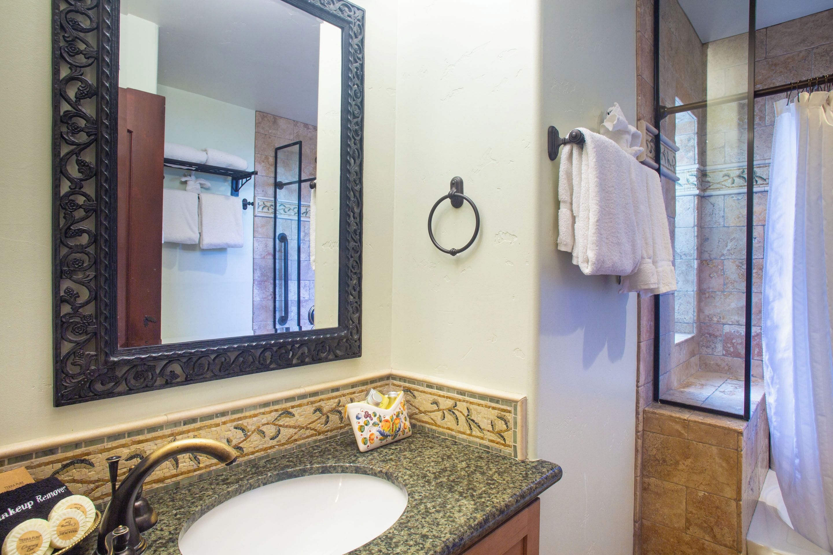 A bathroom with a granite countertop, a sink, a mirror with an ornate frame, a towel ring, and a shower area with a glass door.