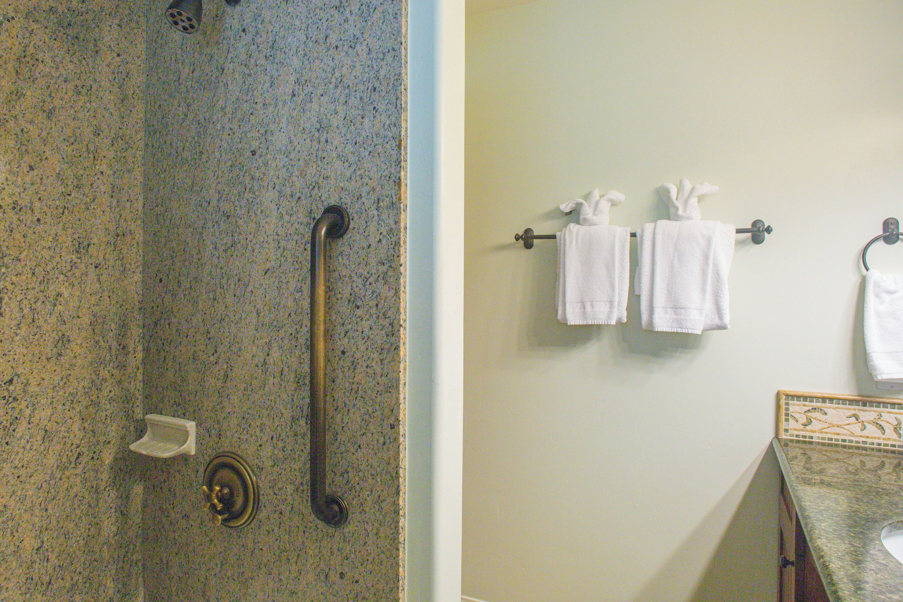 A bathroom with a granite shower, a grab bar, and a towel rack with two white towels.