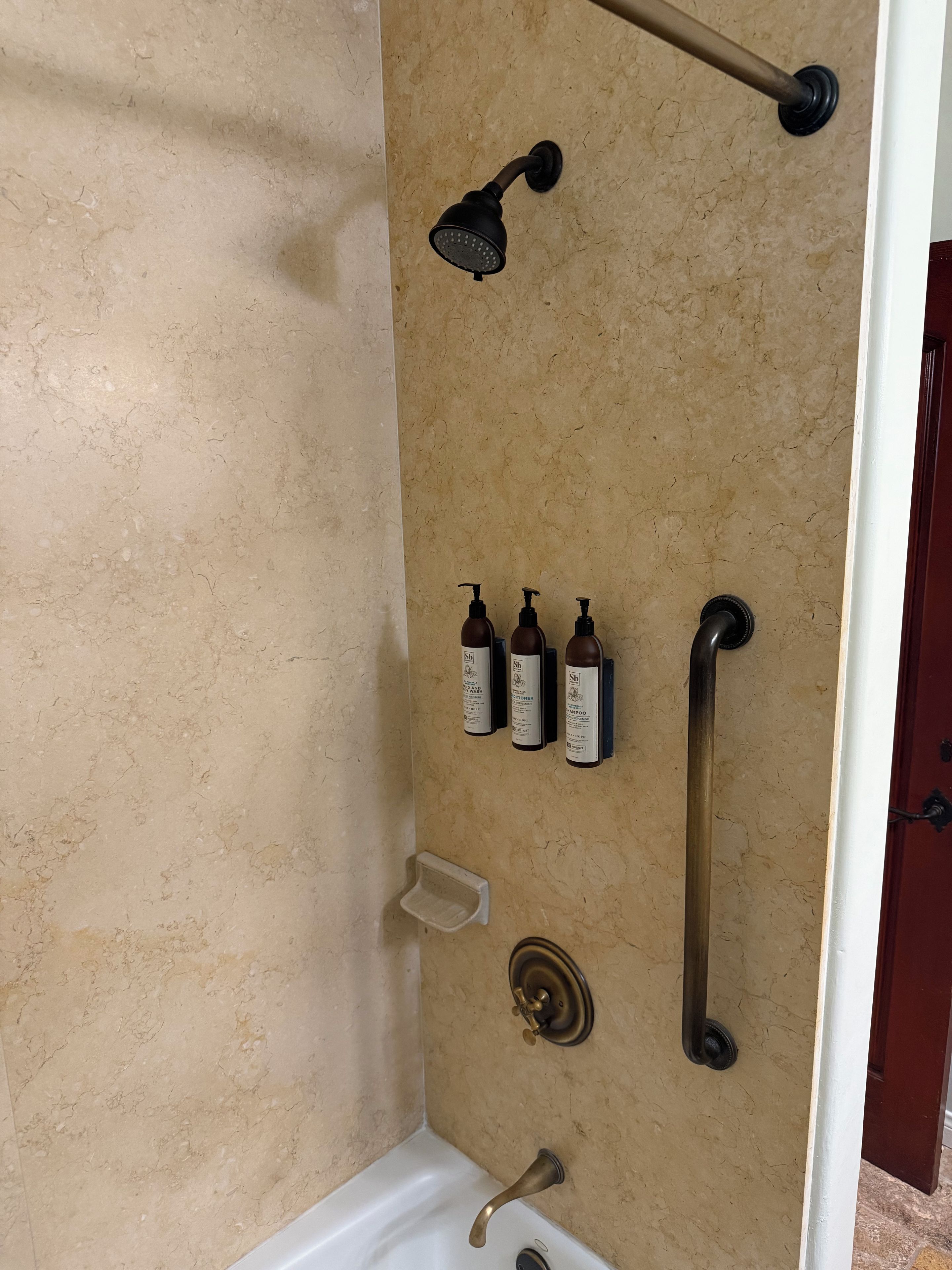 A bathroom with a bathtub, a showerhead, a handheld shower, and three bottles of shampoo.