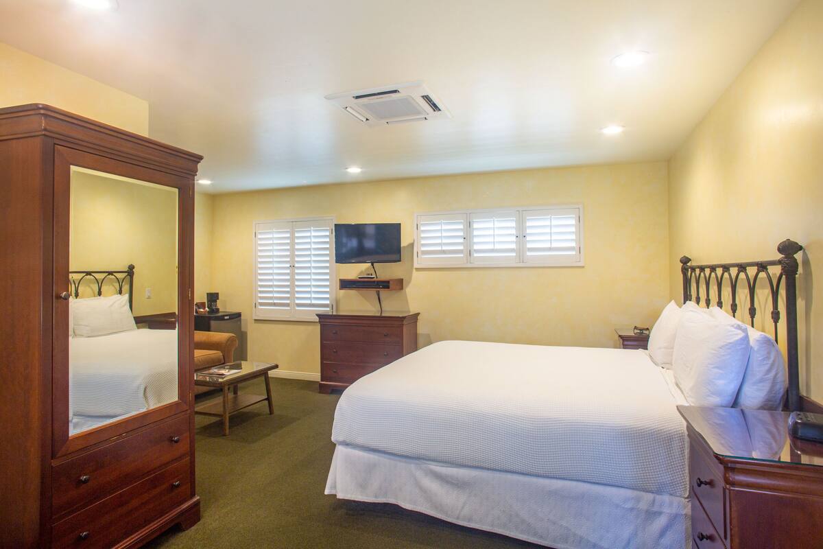 A bedroom with a large bed, a dresser, a television, and a mirror.