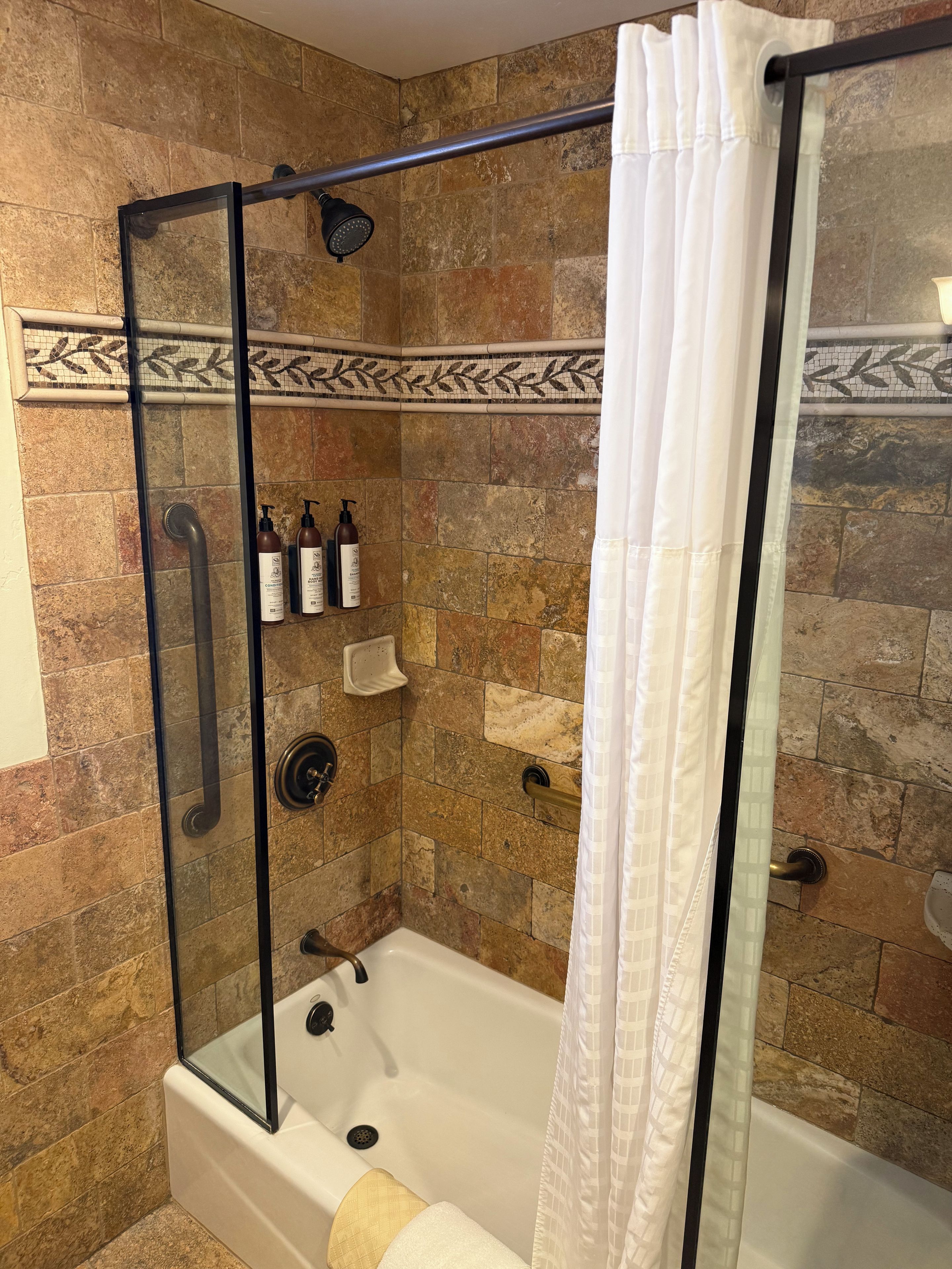 A shower area with a glass door, a white shower curtain, and a tiled wall.