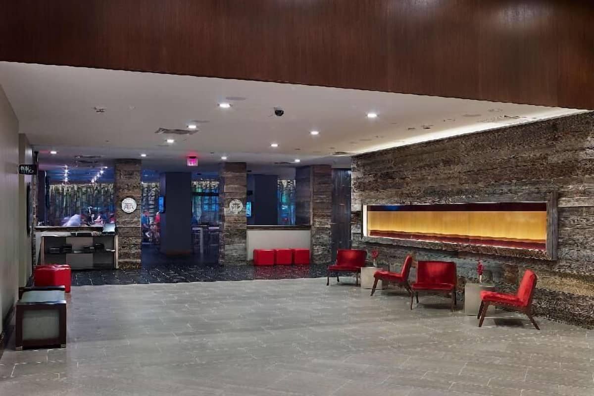 A lobby with a reception desk, red chairs, a stone wall, and a tiled floor.