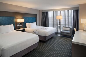 A hotel room with two beds, a desk, a chair, and a large window with curtains.