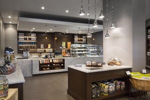 A modern cafe with a marble counter, hanging pendant lights, and shelves stocked with snacks and beverages.