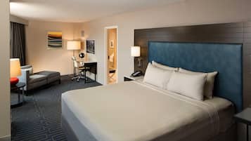 A hotel room with a large bed, a desk with a chair, a small table, and a lamp.
