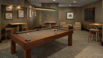 A pool table with balls, surrounded by chairs and tables, in a room with artwork on the walls.