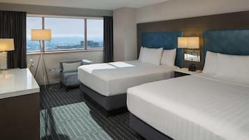 Habitación de hotel con dos camas, un escritorio, una silla, una mesita y vistas a la ciudad.