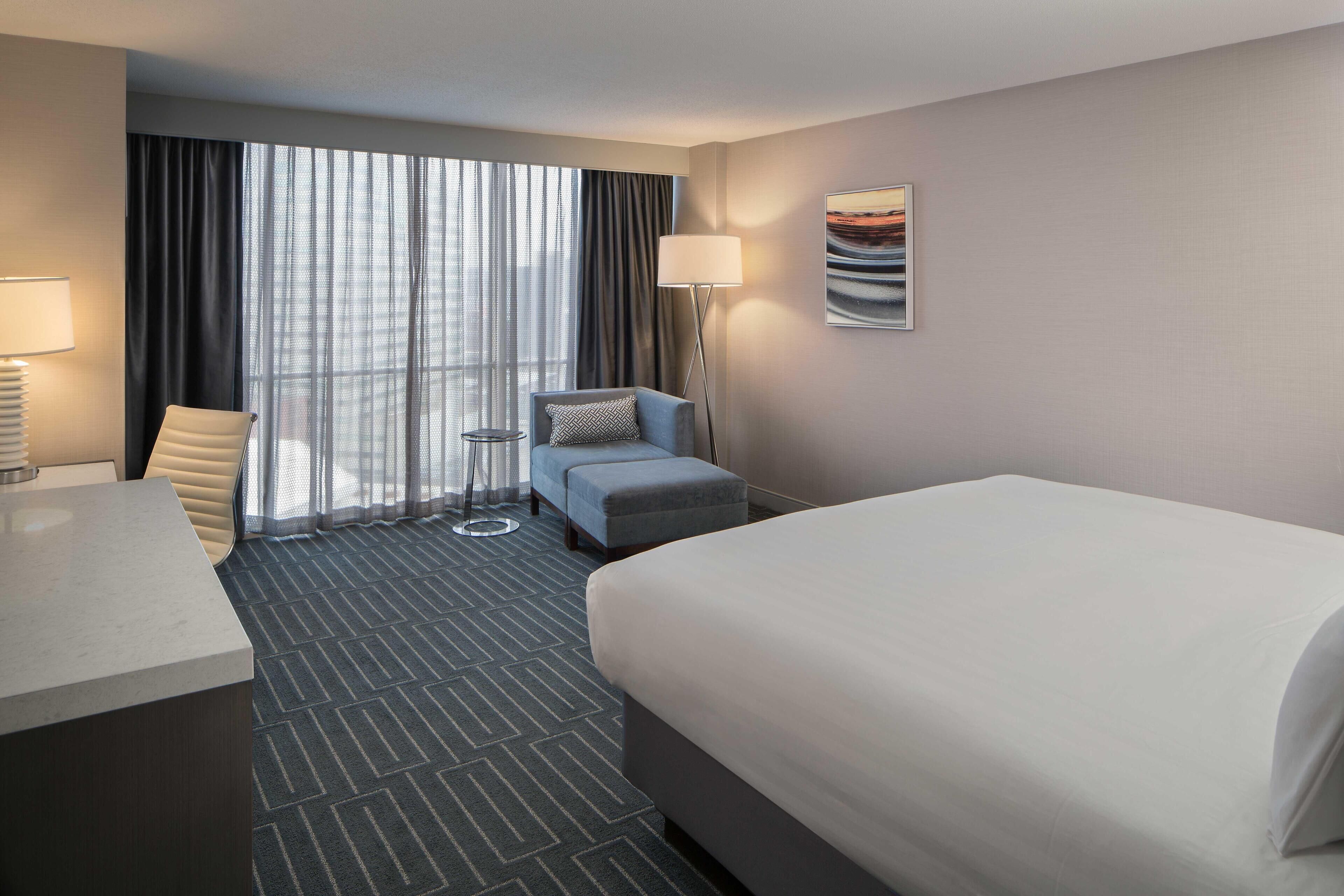Een hotelkamer met een bed, een bureau, een stoel, een bijzettafeltje en een lamp.