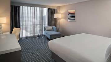 Quarto de hotel com cama, escrivaninha, cadeira, mesa pequena e luminária.