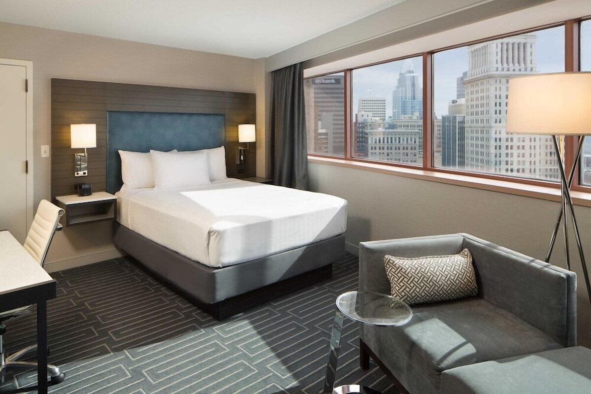 Une chambre d’hôtel équipée d’un lit, d’un bureau, d’une chaise, d’un canapé, d’une lampe et offrant une vue sur le paysage urbain.