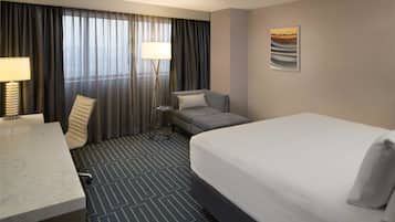 Une chambre d’hôtel avec un lit, un bureau, une chaise, une lampe sur pied et un tableau au mur.