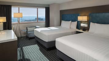 Habitación de hotel con dos camas, un escritorio, una silla, una mesita y vista a la ciudad.