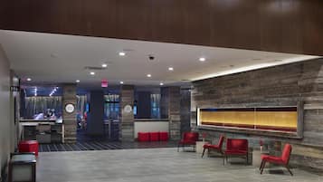 Un vestíbulo moderno con una mesa de recepción, asientos rojos y una pared decorativa de piedra.