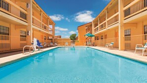 A swimming pool with lounge chairs and umbrellas, surrounded by multi-story buildings with balconies. - Baymont by Wyndham Lubbock - Downtown Civic Center (Lubbock)