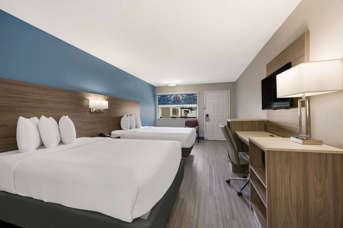 A hotel room with two beds, a desk, a TV, and a window with a view.