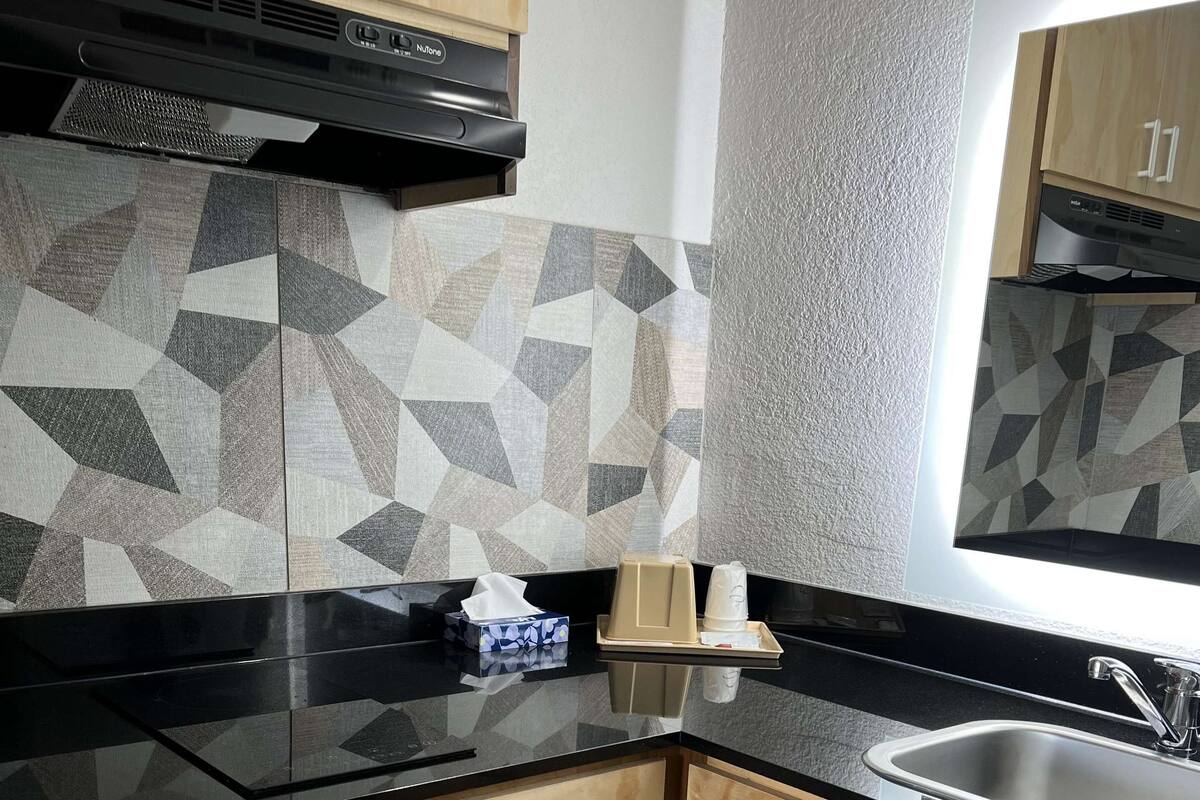A modern kitchen with a black countertop, wooden cabinets, and a geometric tile backsplash.