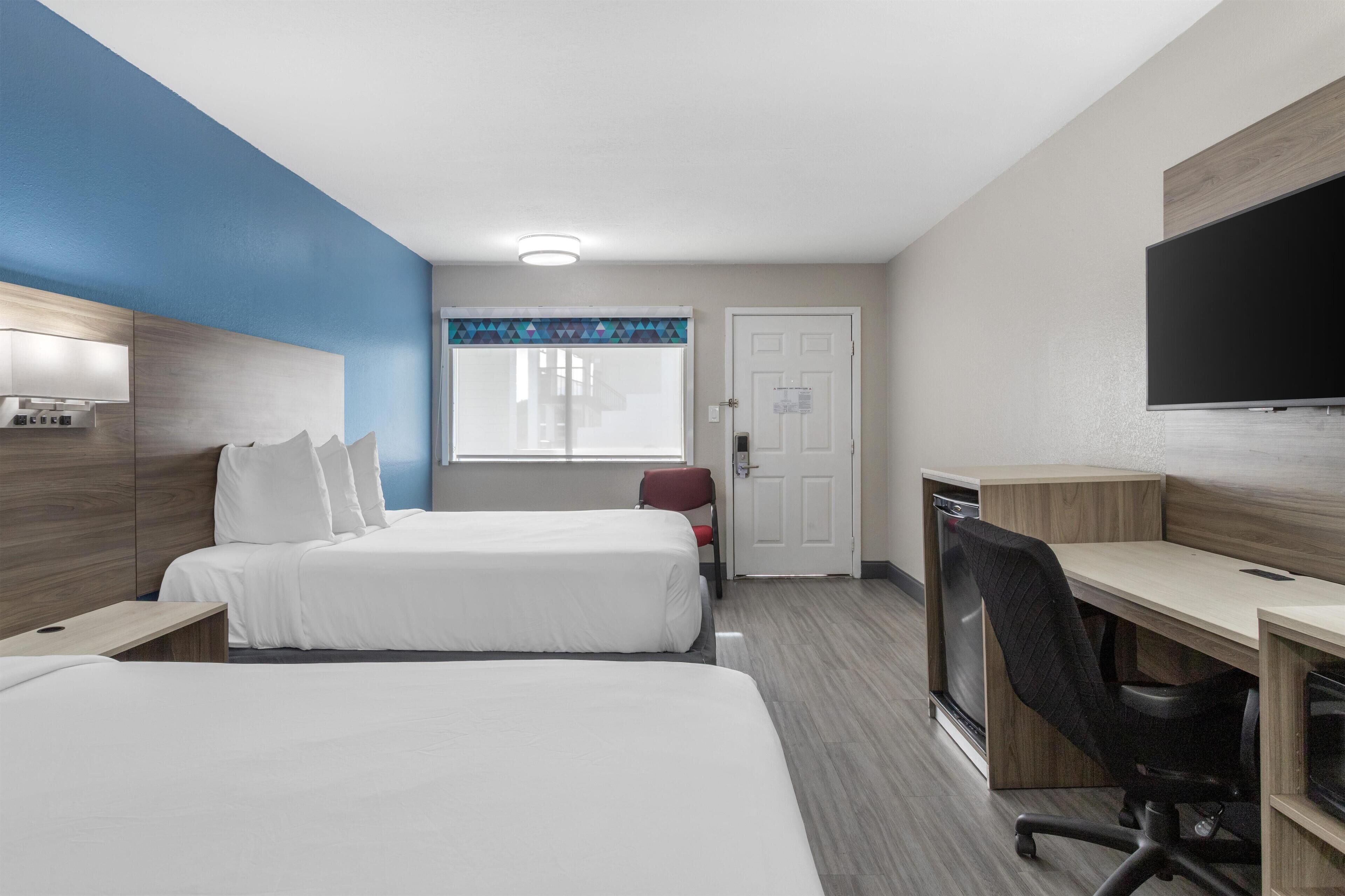 Habitación de hotel con dos camas, un escritorio, una silla, un televisor y una ventana con cortinas.