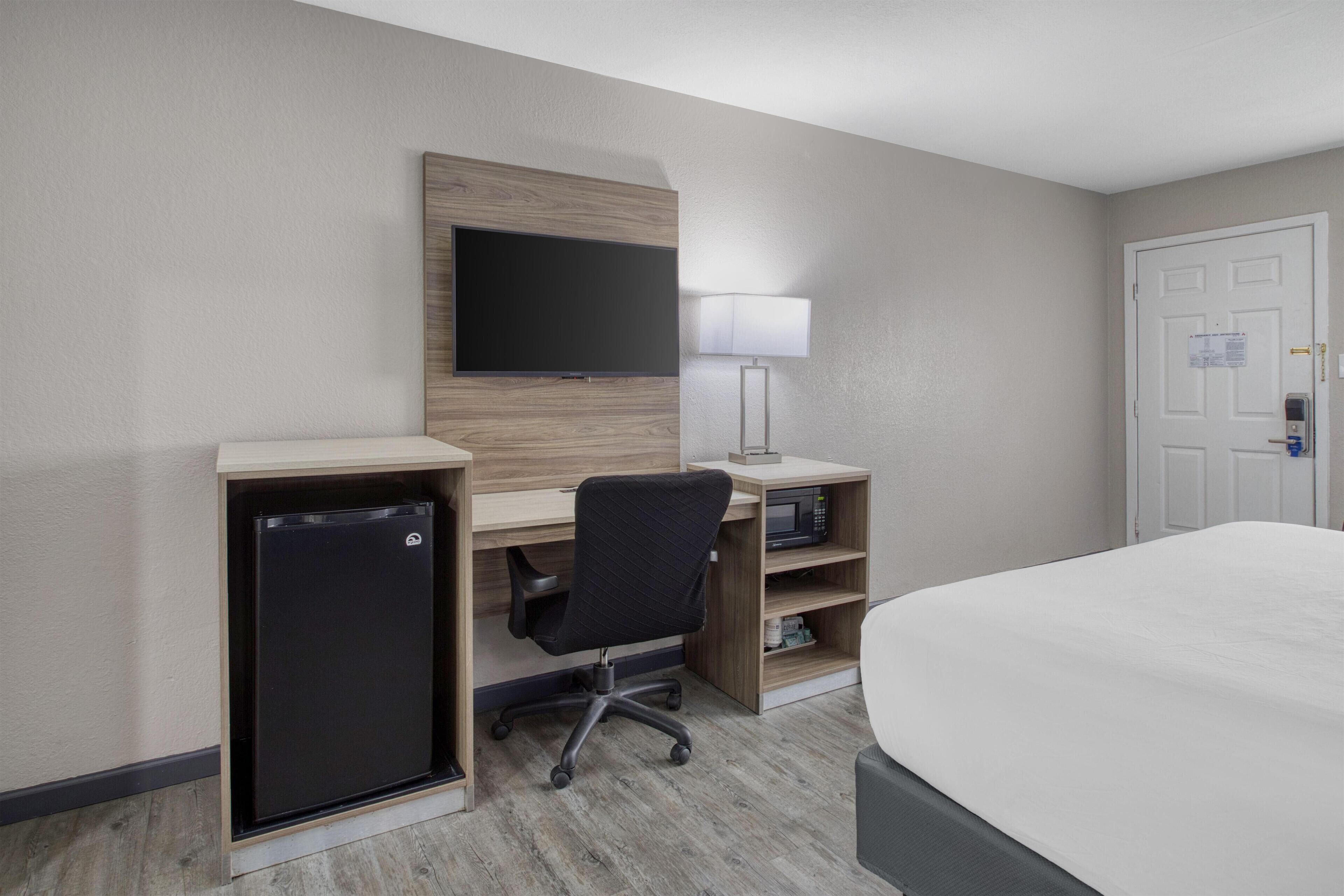 Une chambre d’hôtel équipée d’un lit, d’un bureau avec un ordinateur, d’une télévision, d’un réfrigérateur et d’une lampe.