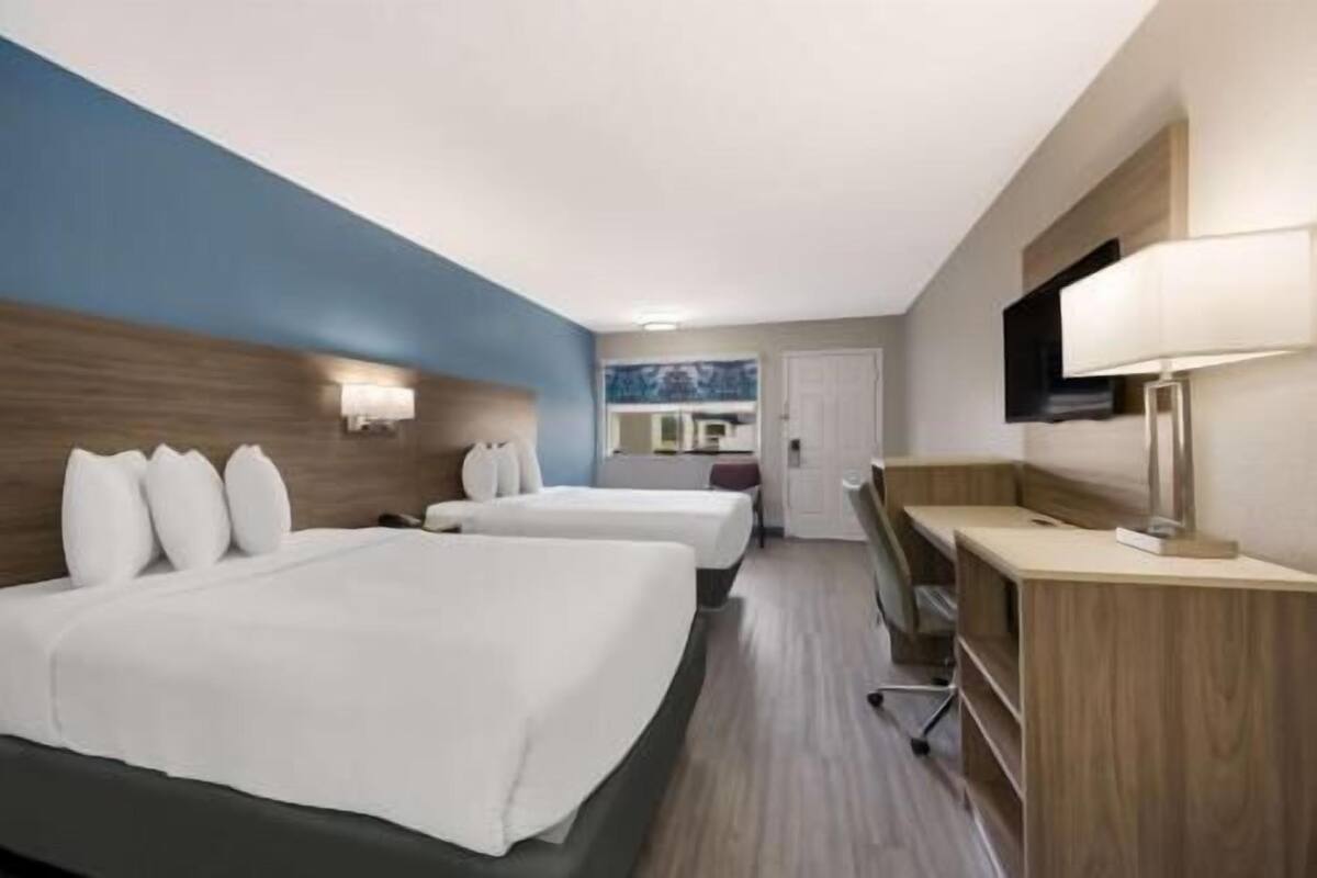A hotel room with two beds, a desk, a chair, a TV, and a bathroom.