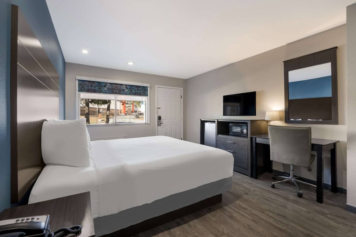 A hotel room with a bed, desk, chair, TV, and a window with a view of the outside.