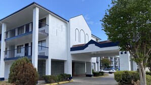 A multi-story building with a white facade, balconies, and a covered entrance.