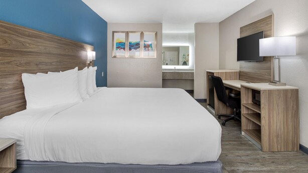 A hotel room with a large bed, a desk, a chair, a TV, and a bathroom visible through a door.