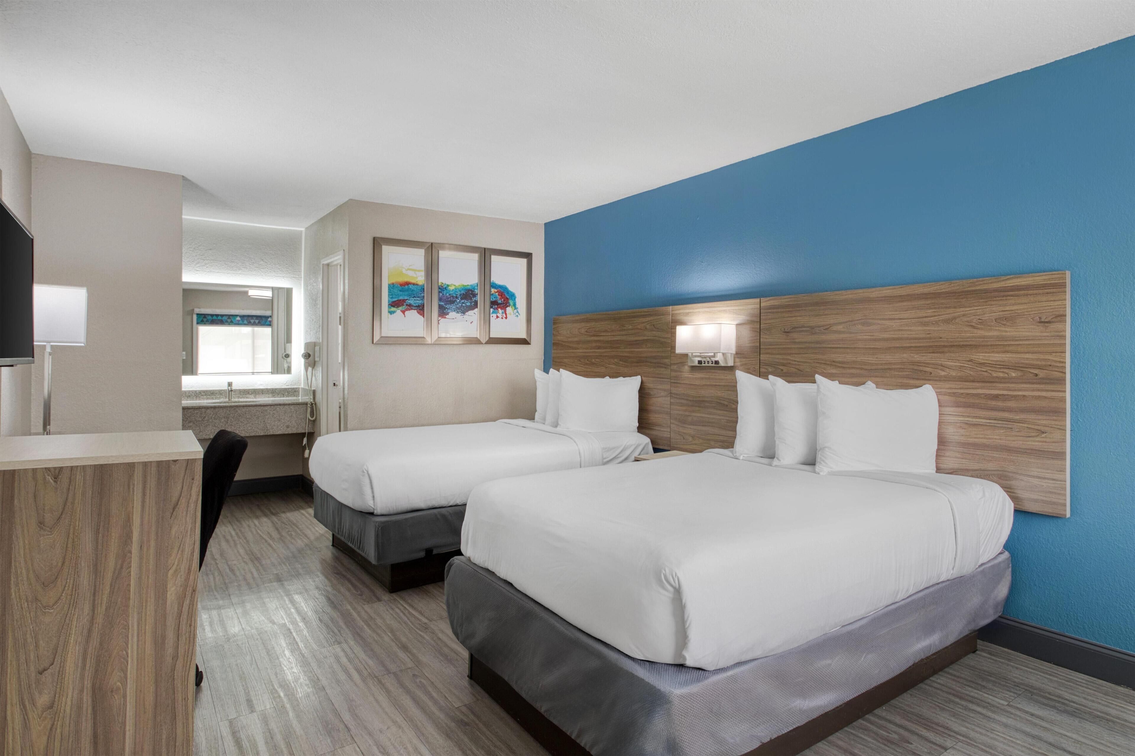 A hotel room with two beds, a wooden headboard, a TV, and artwork on the wall.