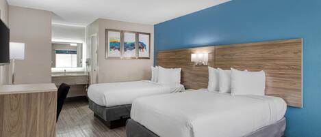 A hotel room with two beds, a wooden headboard, a TV, and artwork on the wall.