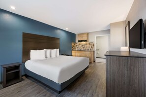 A modern hotel room with a large bed, a wooden headboard, a built-in wardrobe, a small bedside table, and a flat-screen TV. - SureStay Hotel by Best Western Spring North Houston (Spring)
