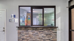 Een receptiegedeelte met een stenen muur, een raam met uitzicht op een winkel en een deur aan de linkerkant.