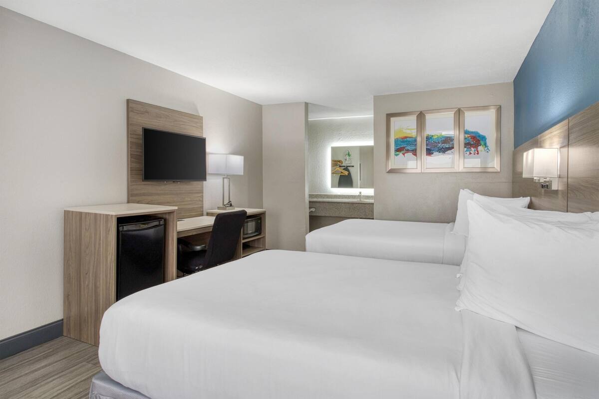 A hotel room with two beds, a desk with a chair, a television, and artwork on the wall.