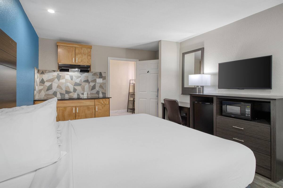 A hotel room with a bed, a TV, a microwave, a desk, and a kitchenette.
