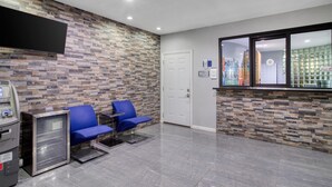 Een receptie met een wand met steenmotief, een flatscreen televisie, twee blauwe stoelen, een glazen vitrine en een deur met een bordje.
