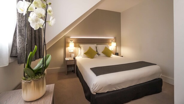 Ein Hotelzimmer mit Bett, Nachttischen, Lampen und einer Topf-Orchidee.