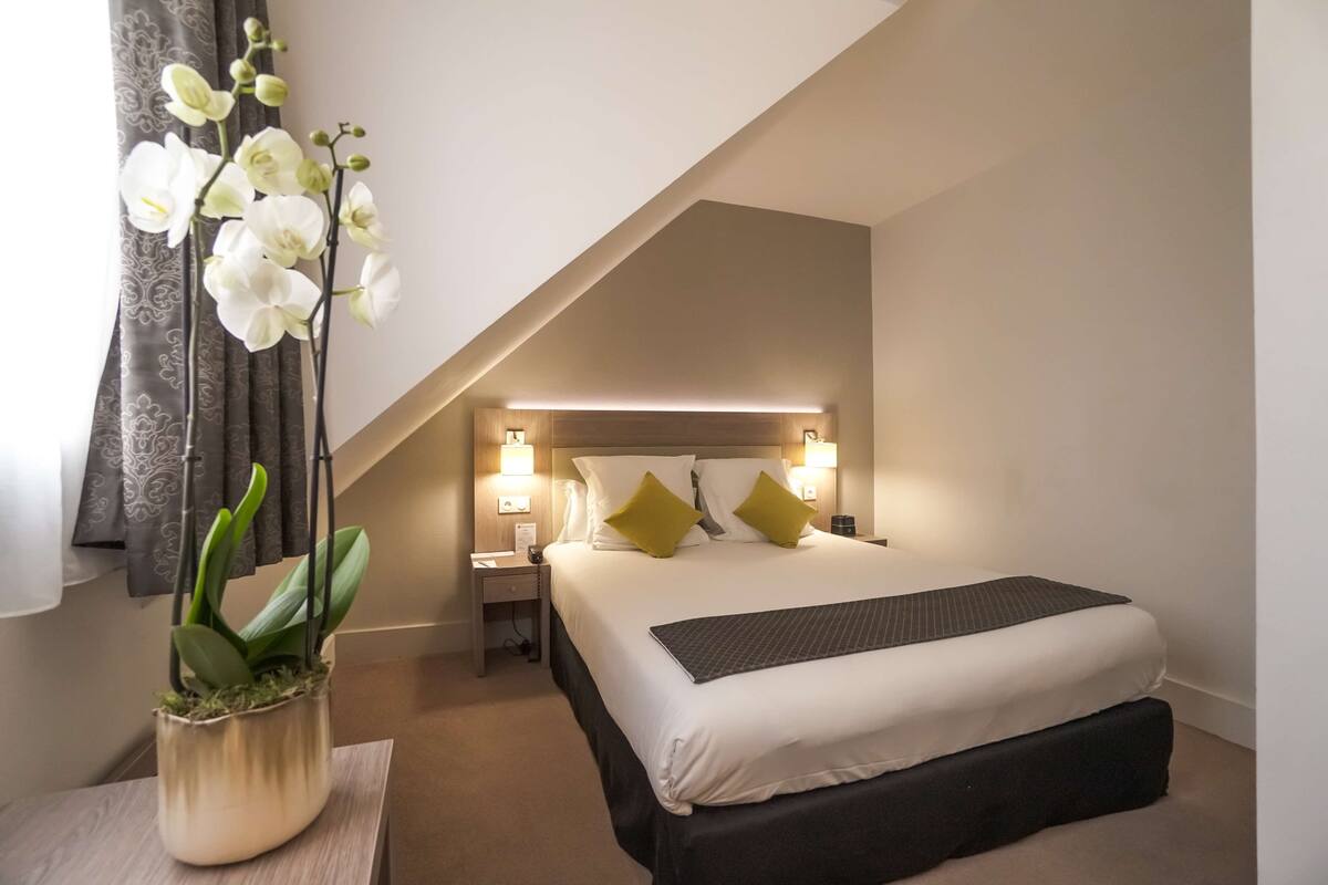 A hotel room with a bed, bedside tables, lamps, and a potted orchid.