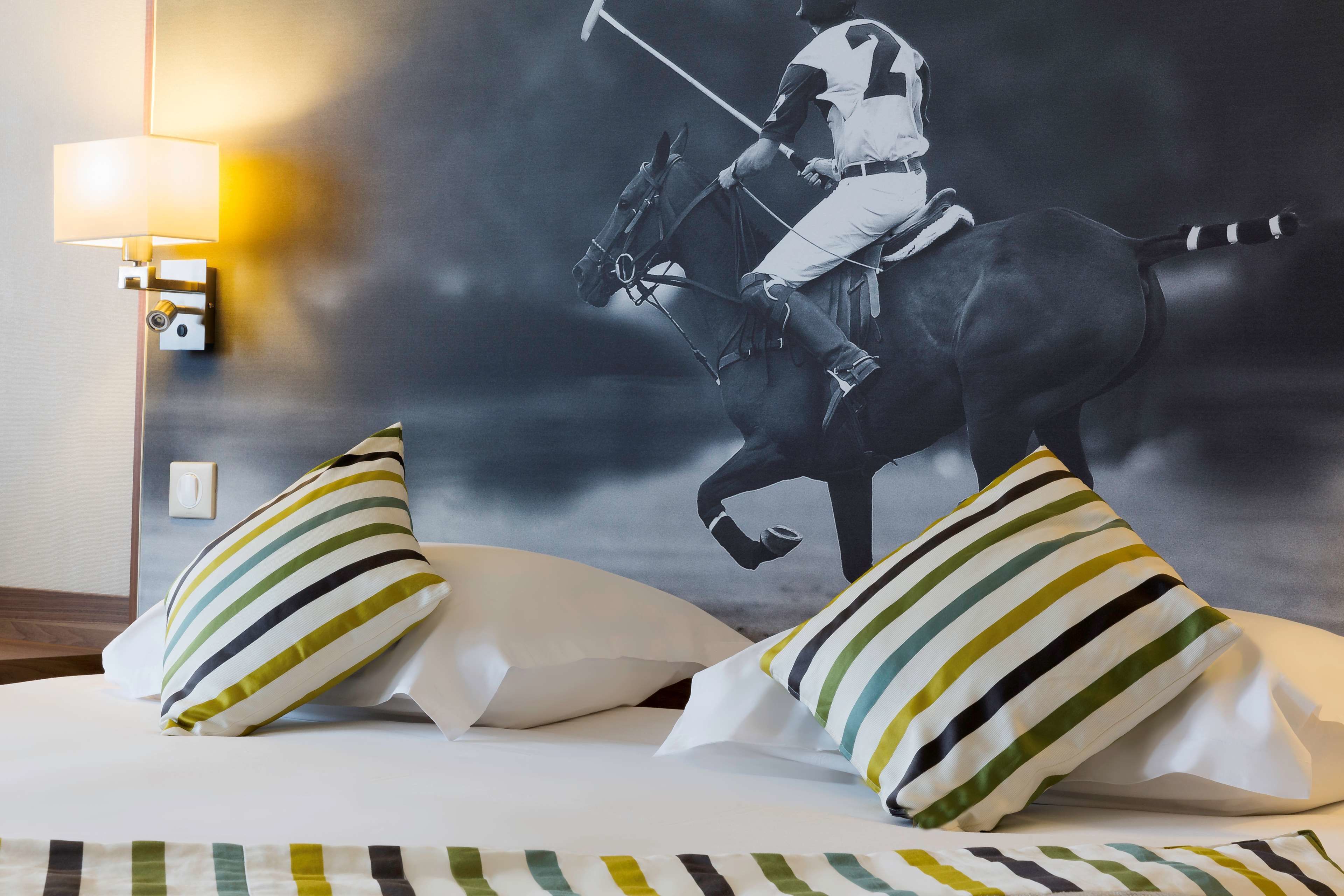 Une chambre d’hôtel avec un lit, des oreillers à rayures et une fresque murale représentant un joueur de polo à cheval.