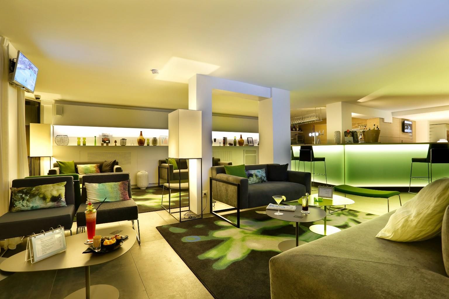 A modern hotel lobby with seating areas, a bar, and a reception desk.