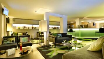 A modern hotel lobby with seating areas, a bar, and a reception desk.