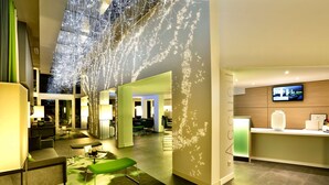 Eine moderne Hotelhalle mit Empfangstresen, Sitzgelegenheiten und einer großen digitalen Anzeige.
