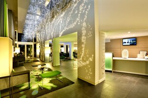 Un moderno vestíbulo de hotel con mostrador de recepción, zona de estar y una gran pantalla digital.