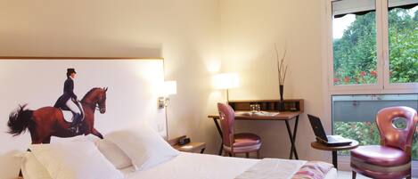A hotel room with a bed, a desk, a chair, and a window with a view of greenery.